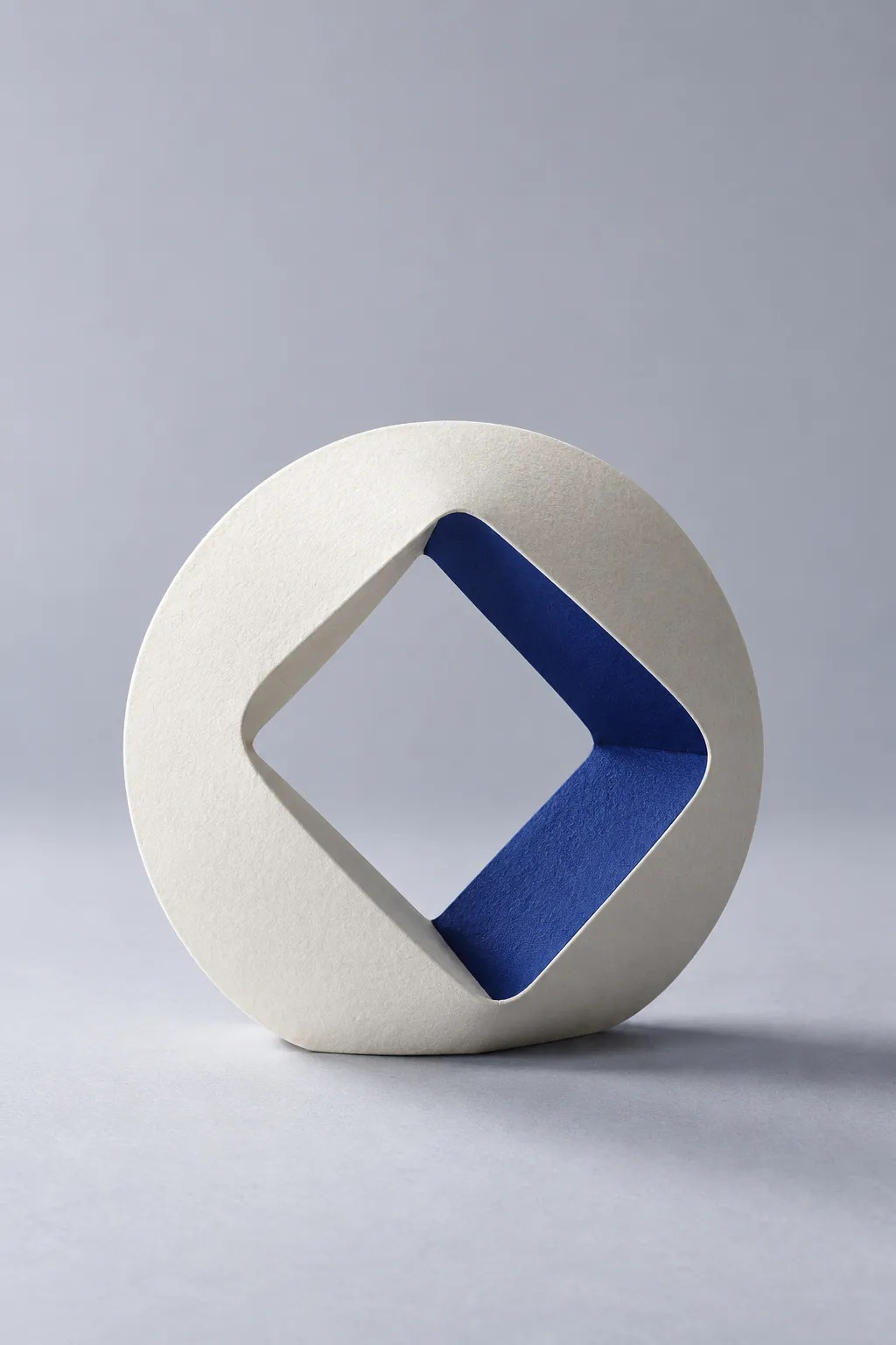 A paper ring folded around a softly rounded square opening, with one indigo facet